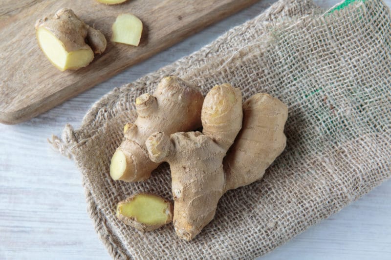 fresh ginger root on top of a burlap napkin with cut ginger in the background