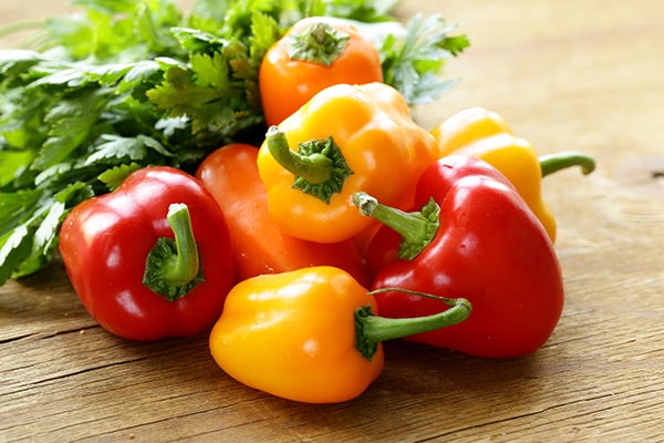 fresh colorful red and yellow bell peppers on a wooden background with fresh cilantro in the background