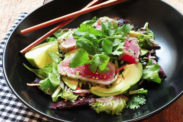 a black bowl with seared tuna on a bed of mixed greens with chopsticks on the side