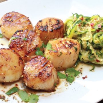 Pan-seared scallops on a white plate with a side of zucchini noodles