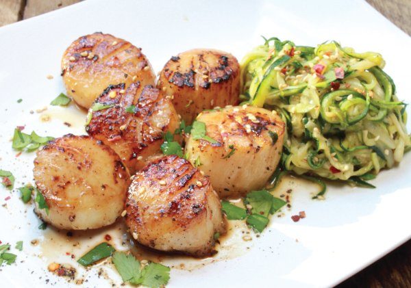 Pan-seared scallops on a white plate with a side of zucchini noodles