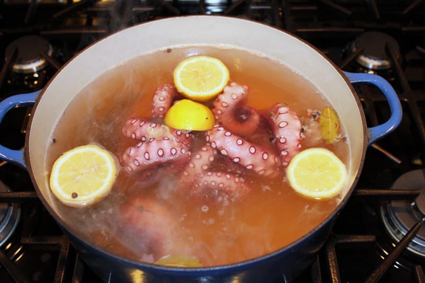 Octopus being boiled in a stock pot with fresh lemon halves and herbs.