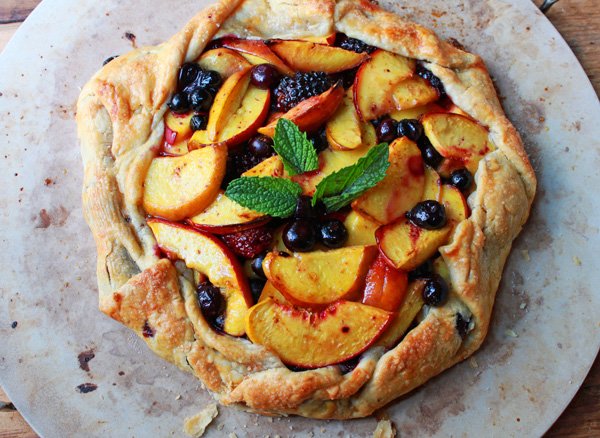 A summer fruit tart pastry with berries and peaches on a white serving plate.