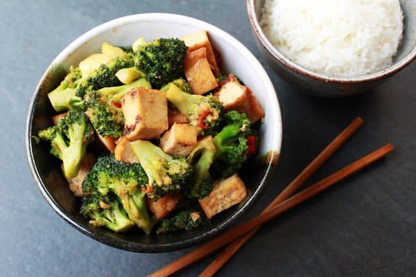 a bowl filled with stir-fry broccoli and tofu cubes with a side of white rice