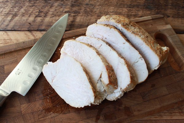 sliced turkey breast on top of a wooden cutting board with a chef's knife along side