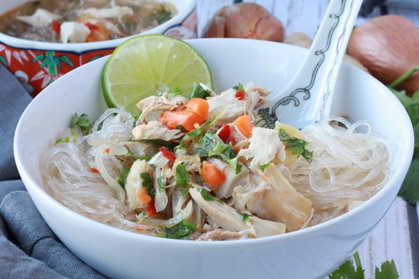 A white bowl filled with Asian turkey noodle soup with rice noodles and chunks of turkey on top with an Asian soup spoon inserted and a slice of lime.