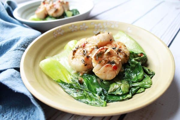 Seared scallops on a plate over a bed of baby bok choy with a blue napkin on the side.
