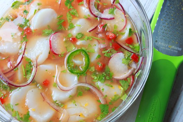 sea scallops marinating in a glass bowl with citrus juices, onions, radishes, and peppers