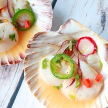 Spicy scallop ceviche presented in pretty shell bowls placed on top of a white wooden board.