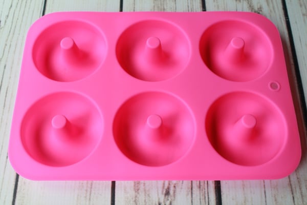 a pink silicone donut tray on a white wooden board