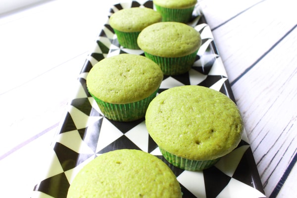 Unfrosted matcha green tea cupcakes on a black and white rectangular plate on top of a white plank wooden board.