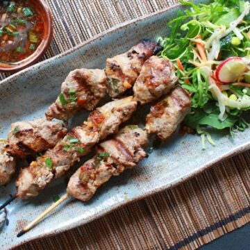 Vietnamese pork tenderloin skewers on a long blue platter with a side salad and dipping sauce on the side.