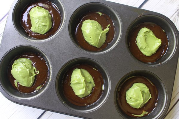 Matcha cheesecake muffin batter layered in a muffin tin ready to be baked in the oven.