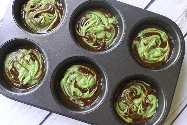 Swirled matcha cheesecake muffin batter layered in a muffin tin ready to be baked in the oven.