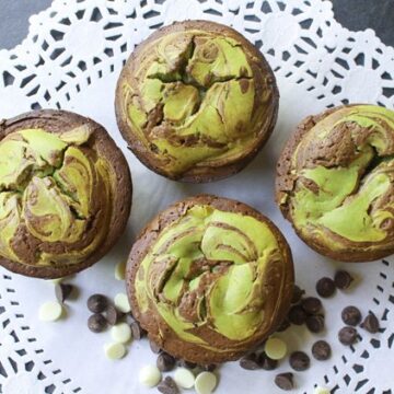 Matcha cheesecake muffins on top of a white doily with chocolate chips on the side.
