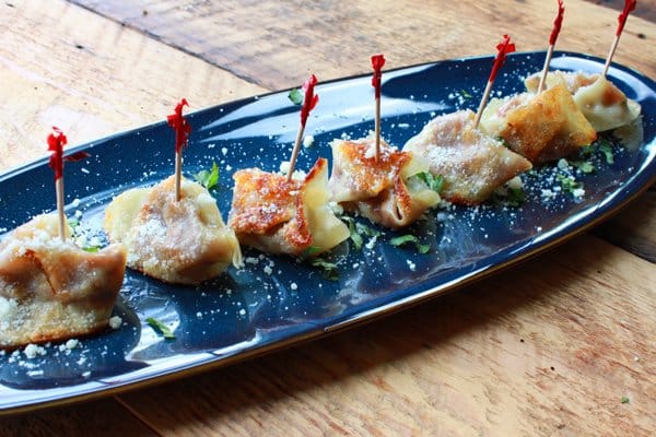 Savory pumpkin wonton bites topped with serving toothpicks prepared on a blue serving platter on top of a wooden board.