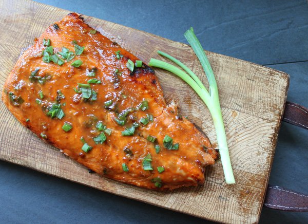 miso glazed salmon filet on a wooden board with a green onion along side