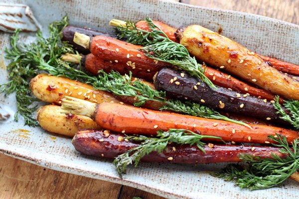 roasted rainbow carrots with tops on placed on a white and beige oval plate on a wooden board