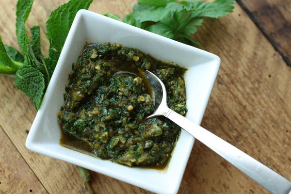 Easy Thai herb sauce in a white square bowl with a silver spoon with sprigs of mint and cilantro on a wooden board