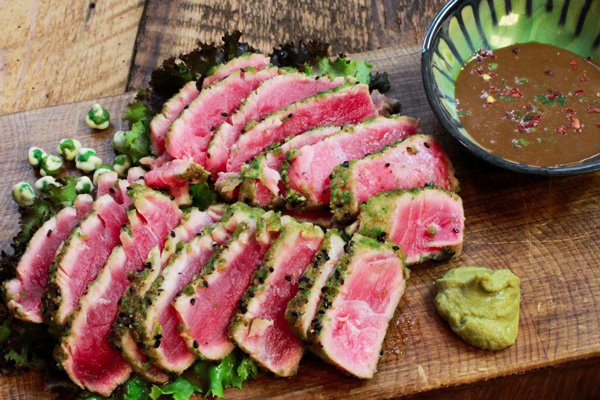 seared tuna slices on a wooden cutting board with a side of dipping sauce and wasabi