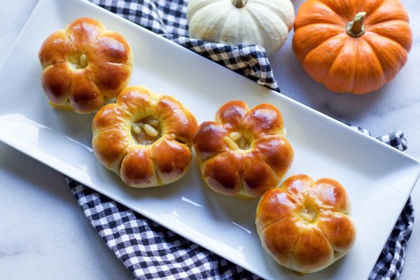 Pumpkin-shaped manju sweets displayed on a long white platter on top of a checkered napkin with a two baby pumpkins on the side. 