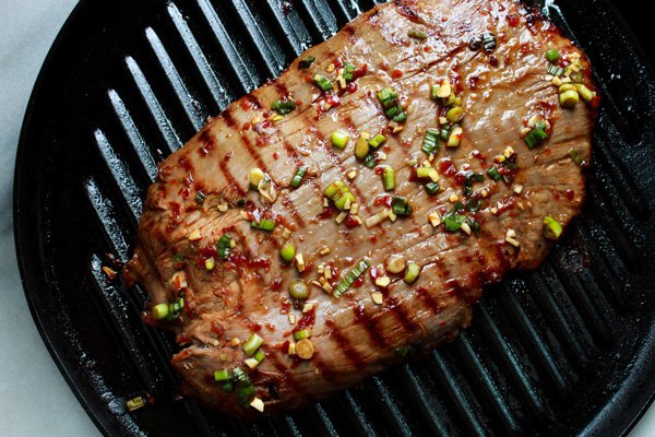 Whole flank steak on a grill pan topped with garlic and scallions.