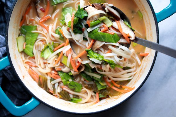 Miso chicken noodle soup in a blue stock pot with a ladle inserted in it on top of a marble surface.