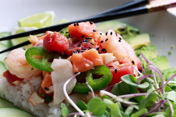 Mixed seafood poke bowl with fresh sushi-grade fish, with black chopsticks and radish sprouts on the side.