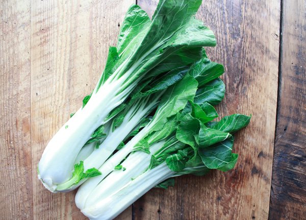 two bunches of bok choy on a wooden cutting board