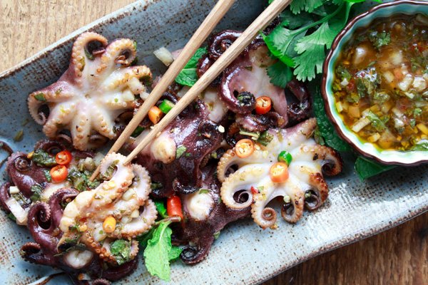 grilled baby octopus on a plate with nuoc cham dipping sauce on the side and chopsticks