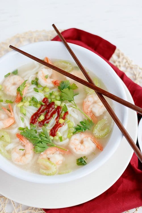 A white bowl of spicy Asian shrimp soup with a pair of brown chopsticks on top of the bowl with a red napkin underneath the bowl.