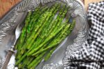 Vibrant grilled asparagus spears on a silver serving platter with a black and white checkered napkin on the side.