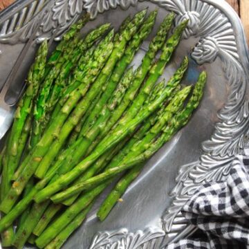 Vibrant grilled asparagus spears on a silver serving platter with a black and white checkered napkin on the side.