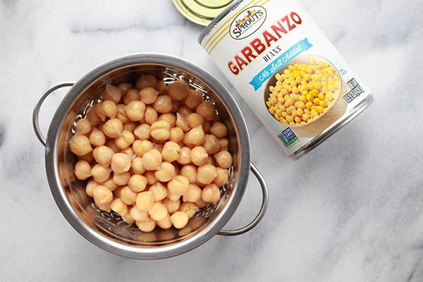 chickpeas garbanzo beans in a silver strainer with a can of garbanzo beans on the side on top of a marble surface