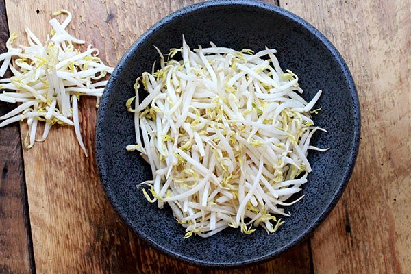 Fresh bean sprouts in a black bowl on top of a wooden board