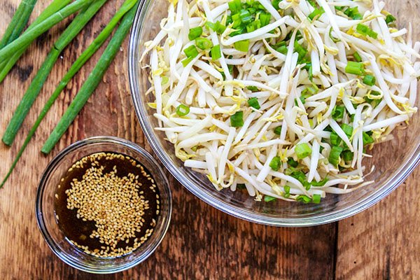 Fresh bean sprouts salad in a glass bowl with green onions and dressing on the side