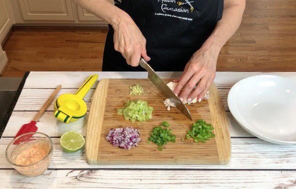 A woman cutting ingredients for making a lobster salad on top of a wooden cutting board.