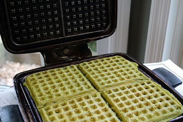 Cooked matcha waffles in a waffle maker with the lid open.