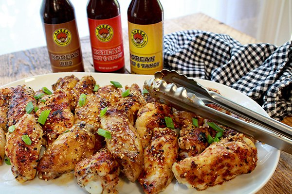 baked Korean chicken wings on a white platter with tongs and three bottled sauces placed behind