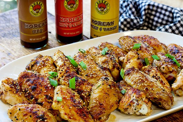 baked Korean chicken wings on a white platter with three bottled sauces placed behind