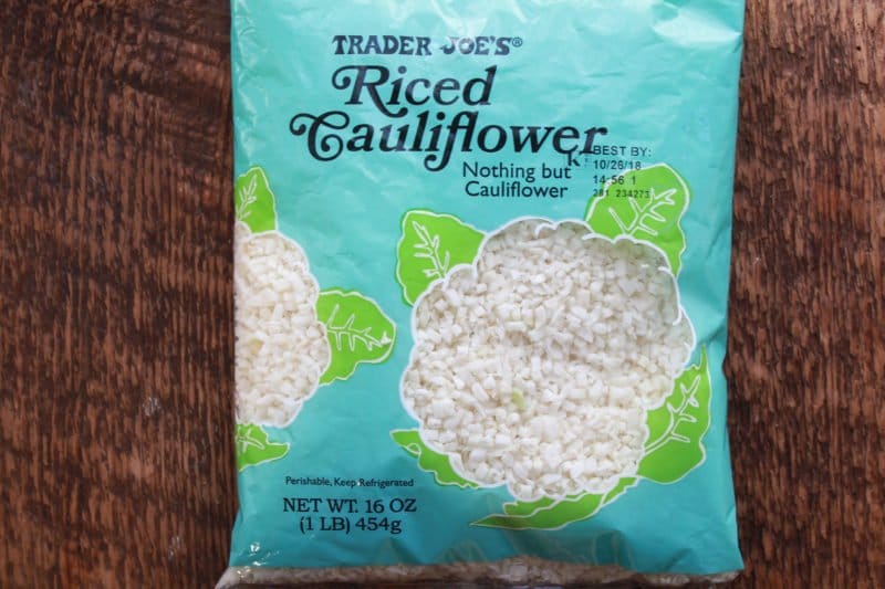 A blue bag of Trader Joe's riced cauliflower placed on top of a wooden board.