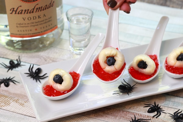 Lychee eyeball jello shots on small white serving spoons and fake spiders along side