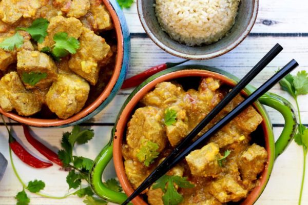 Instant pot coconut curry pork in two bowls with a side of rice and a pair of chopsticks placed on top.