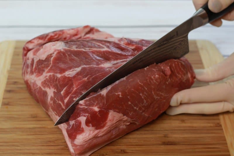 pork butt being sliced on a wooden cutting board