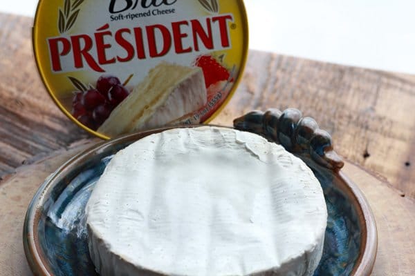 A package of President Brie placed on top of a ceramic blue brie baking plate placed on a wooden board.