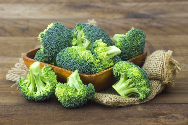 broccoli florets in a brown bowl on a wooden board