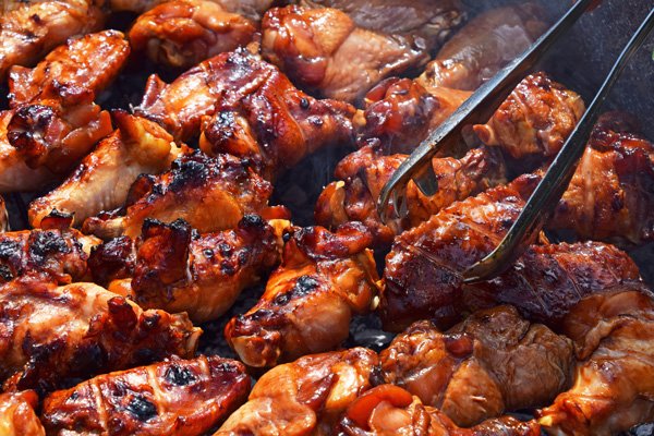 A set of tongs picking up a saucy baked chicken wing with other wings on a platter ready to be served.