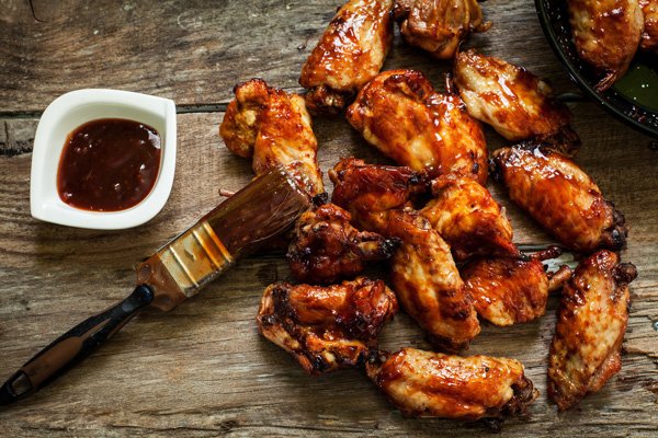 Saucy honey garlic chicken wings on top of a wooden board with a side of sauce and a pastry brush.
