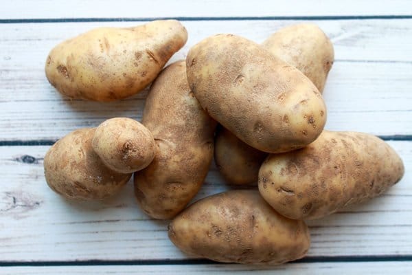 A bunch of Idaho potatoes piled on a white wooden board.