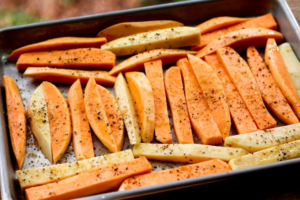 Sweet potatoes wedges placed on a baking sheet and sprinkled with spices read for the oven.